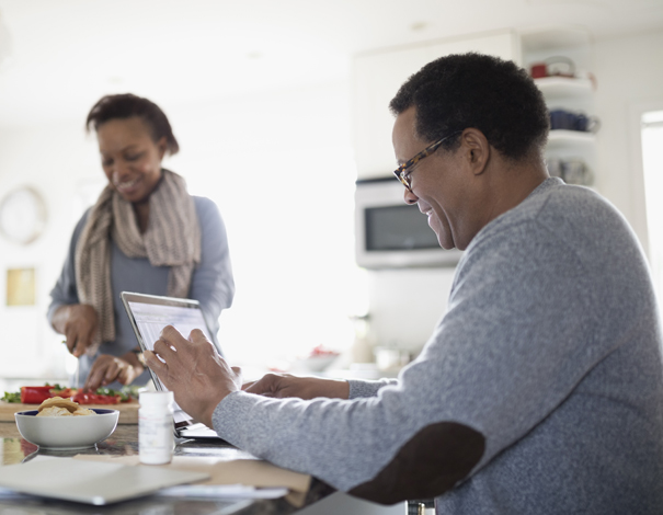 man on ipad while wife is making salad